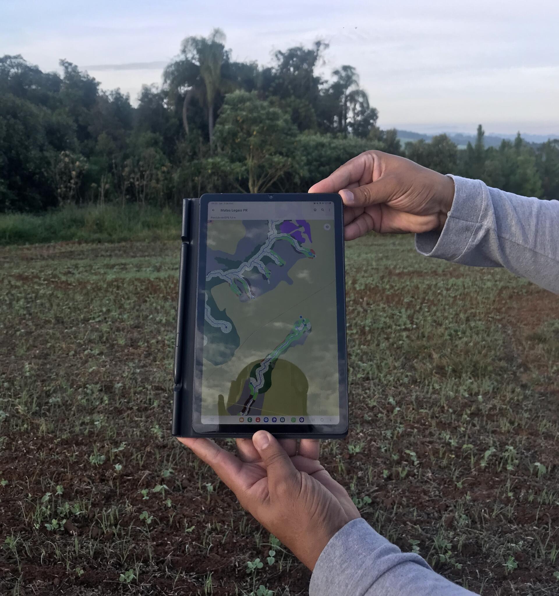 Mapa de uso do solo elaborado no ArcGis e sendo utilizado em campo na semana de campo no Paraná que ocorreu no início de maio de 2023 e ao fundo uma Área de Preservação Permanente em processo de restauração. Foto: Thamara Santos de Almeida